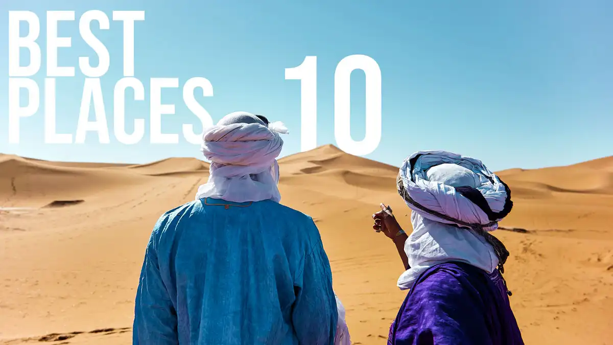 two men in the sahara desert pointing to the best 10 places to visit in morocco as a text on the sand dune