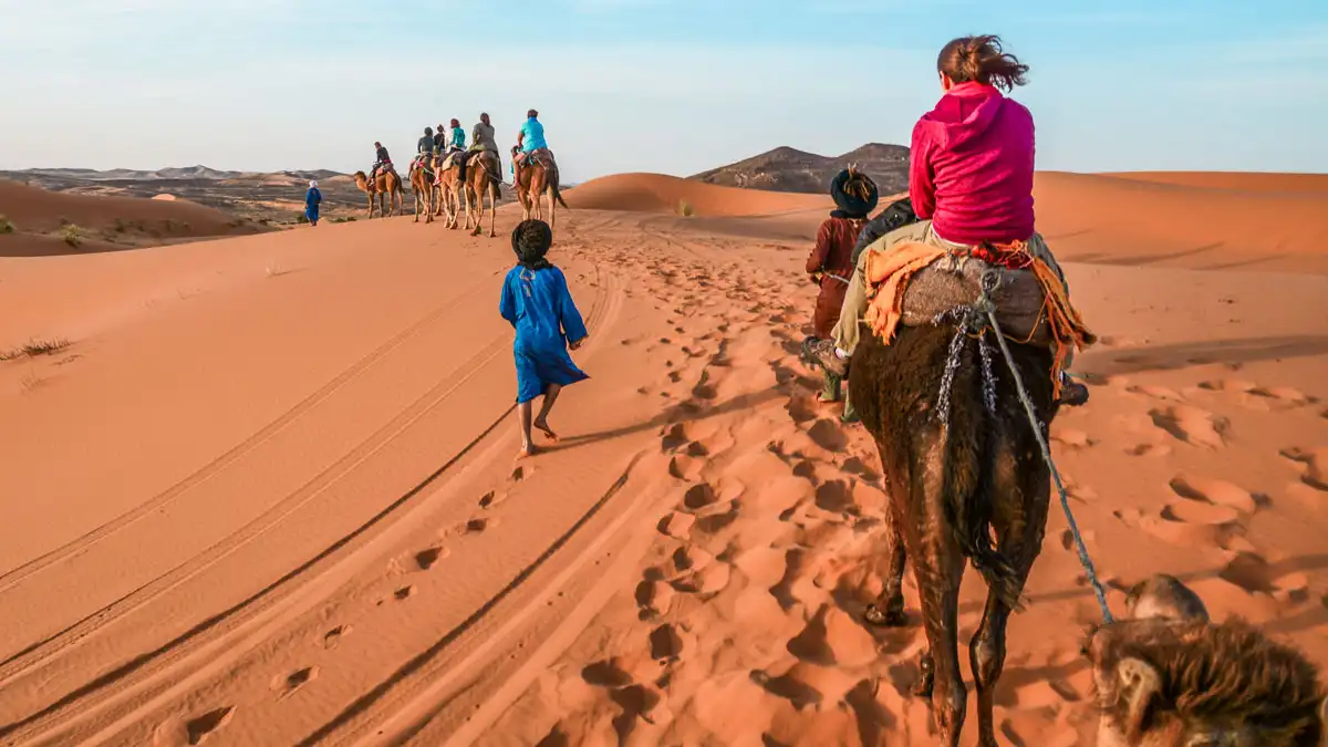 women on a camel with a guide in the desert of morocco