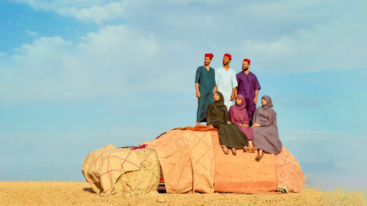 group of moroccan men and women standing on a car in the desert dressing up in traditional moroccan clothes