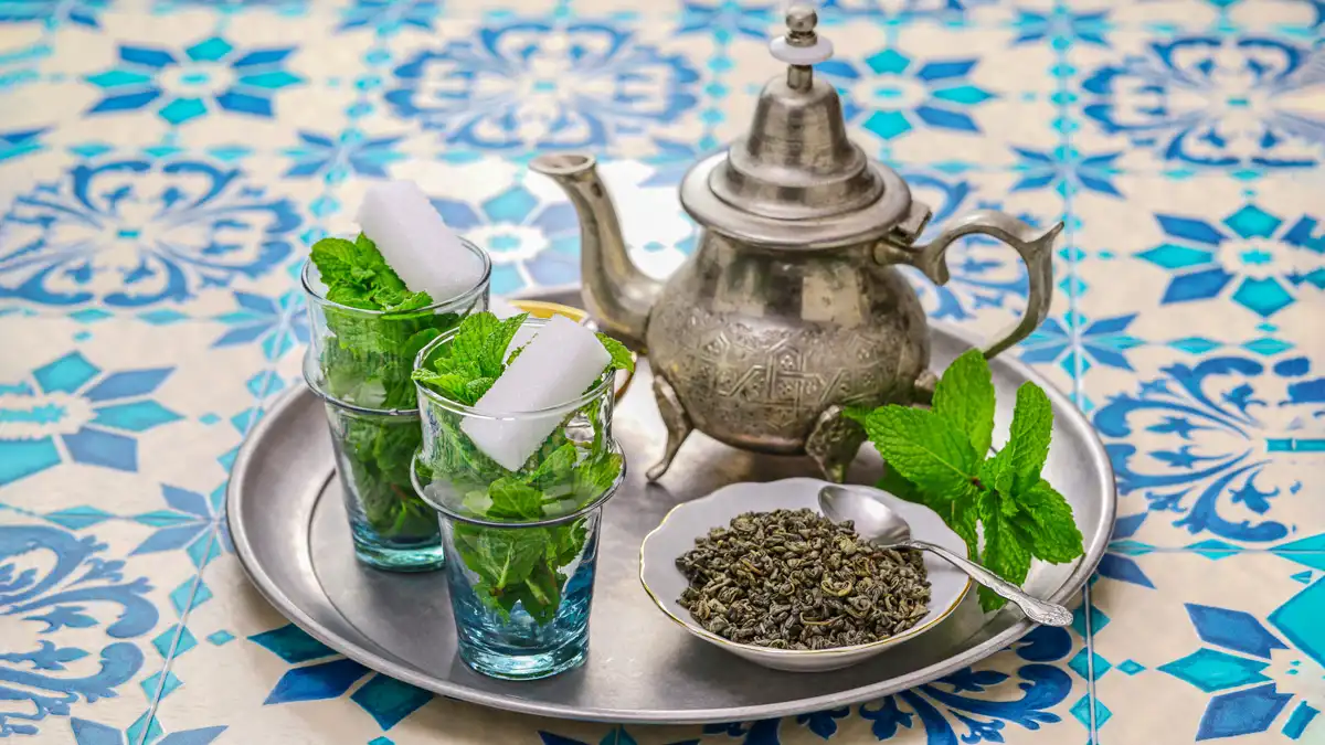 moroccan mint tea in a plate with cups, sugar blocks and fresh moroccan mint