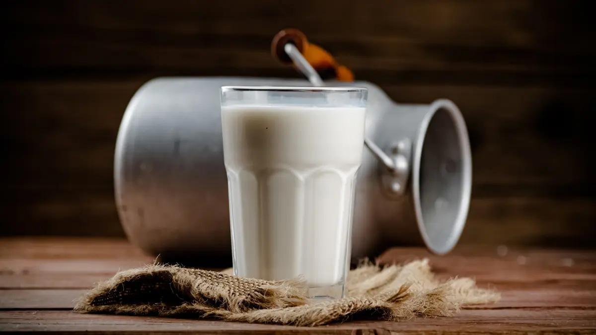 cup of milk lben on the table with a pot behind it